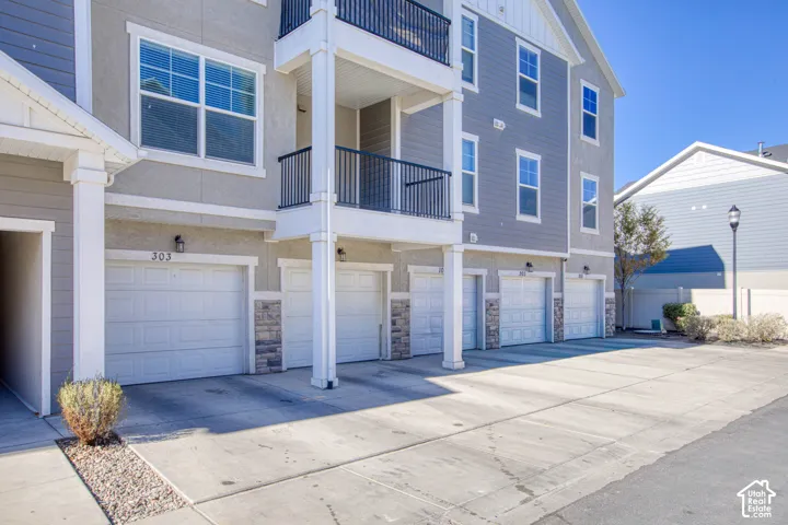 Stucco exterior with stone veneer accents, individual garage doors, and private balconies featuring black metal railings