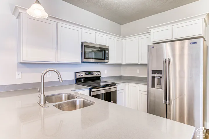 Contemporary kitchen featuring light-toned countertops, white cabinetry with crown molding, a double basin stainless steel sink with a gooseneck faucet, and stainless steel appliances