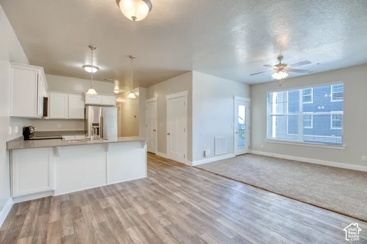 Open-concept living area with wood-finish flooring, white cabinetry, integrated stainless steel appliances, and a ceiling fan