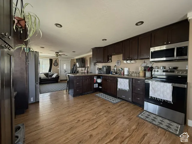 Open-concept kitchen with wood-finish flooring, dark wood cabinetry, stainless steel appliances, and recessed lighting