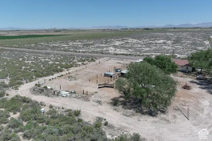 Expansive lot with a single-story residence, mature trees, and outbuildings, featuring a partially fenced perimeter and surrounding arid landscape