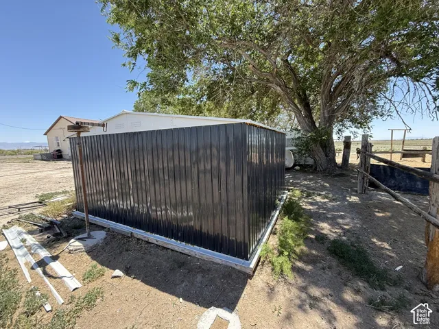 Corrugated metal outbuilding with a white flat roof, surrounded by a natural landscape with a mature tree