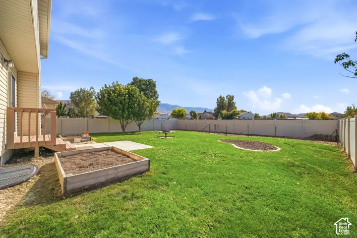 Expansive backyard oasis featuring a generous manicured lawn, raised garden beds, mature shade trees, composite patio area, and vinyl privacy fencing with mountain vistas in the distance