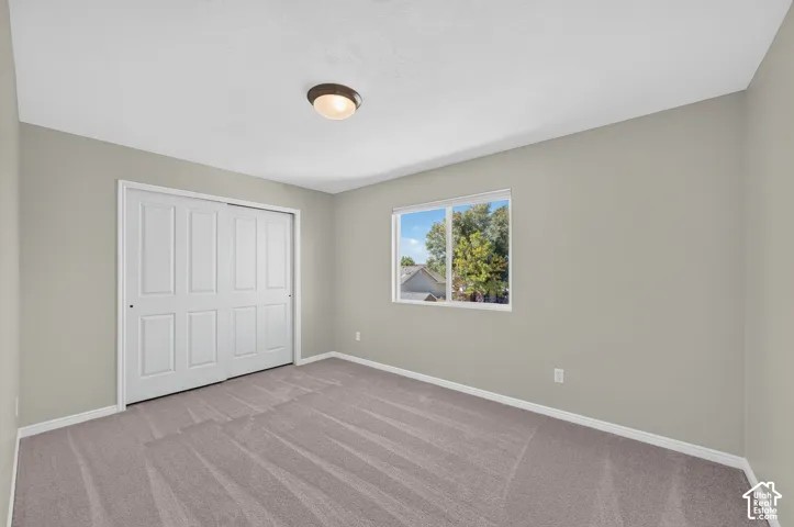 Spacious bedroom with plush carpeting, large window with natural light, white six-panel closet doors, and recessed ceiling lighting