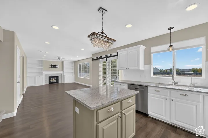 Open-concept living space featuring wood-finish flooring, a kitchen island with stone countertop, white shaker cabinetry, a built-in fireplace, and integrated shelving
