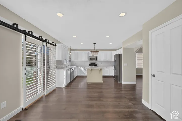 Spacious kitchen featuring white cabinetry, stainless steel appliances, a large center island with pendant lighting, recessed ceiling lights, and wood-finish flooring throughout