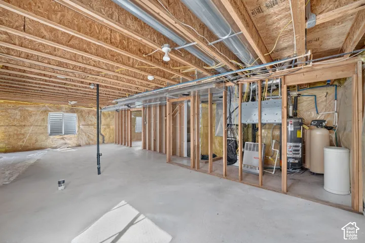 Unfinished basement with exposed ceiling joists, concrete flooring, and framed interior walls, featuring a water heater and water softener