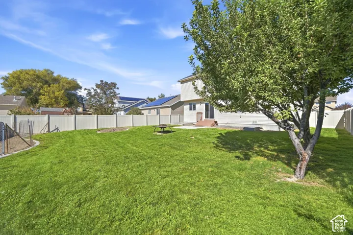 Expansive backyard featuring a manicured lawn, mature shade trees, and vinyl fencing