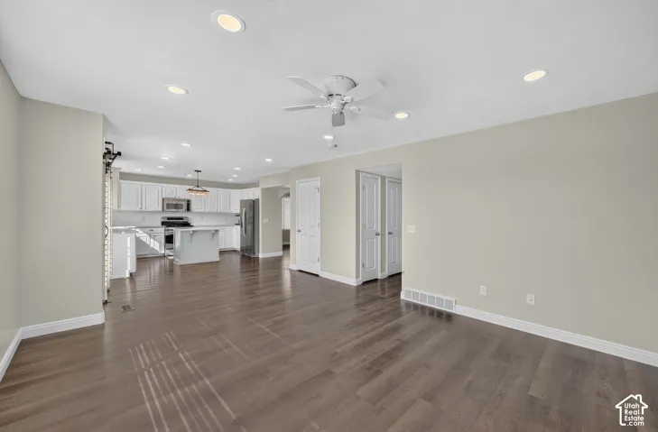 Wood-finish flooring throughout, recessed lighting, white ceiling fan, white kitchen cabinetry, and a center island with pendant lighting