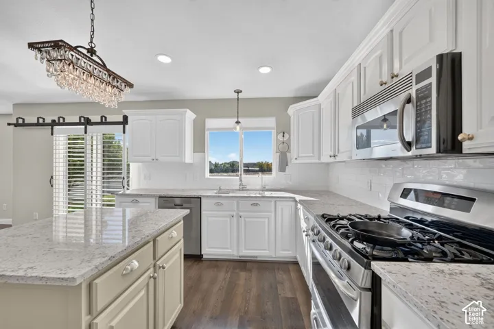 Bright kitchen featuring white cabinetry, light-toned countertops, stainless steel appliances, wood-finish flooring, and a decorative chandelier