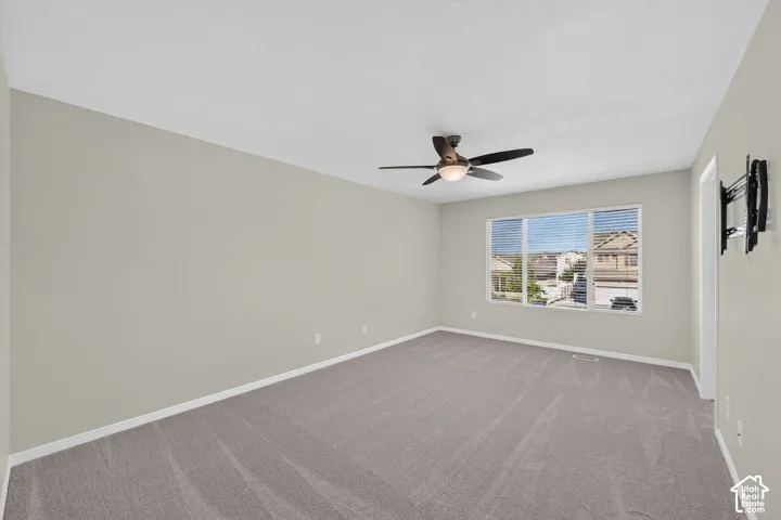 Spacious room featuring gray carpeting, neutral wall paint, a multi-pane window with blinds, and a ceiling fan with integrated lighting