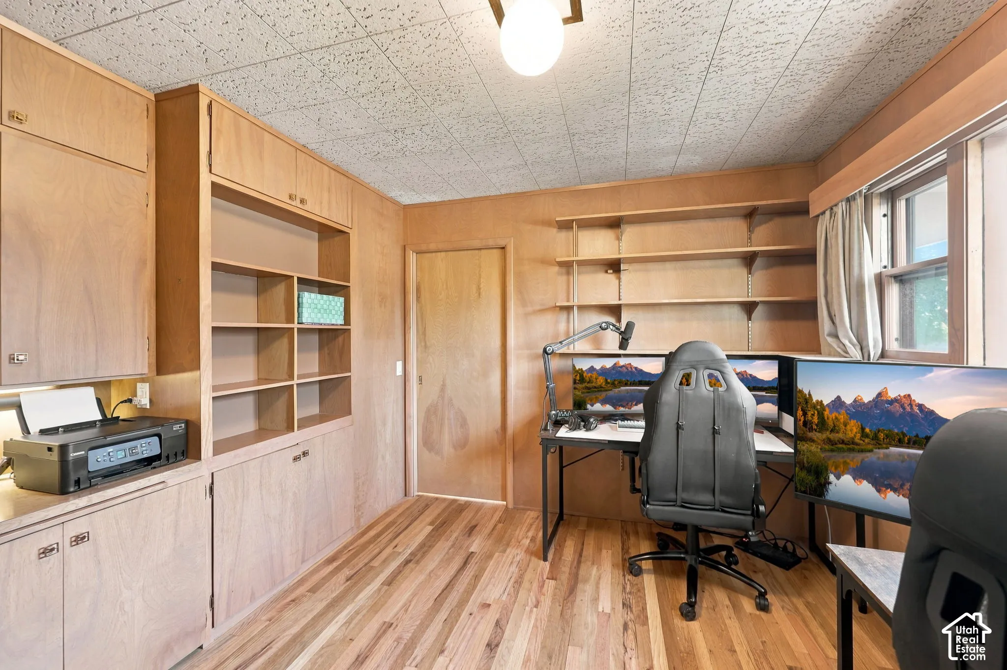 Dedicated home office featuring built-in cabinetry with open shelving, wood-finish flooring, and abundant natural light from dual windows