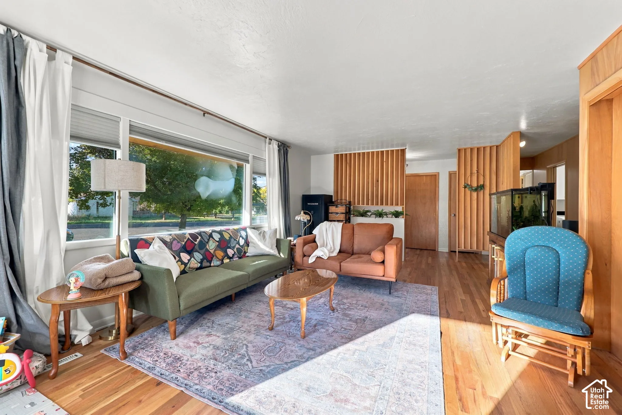 Hardwood flooring throughout, large picture window with roller shades, and natural wood paneling