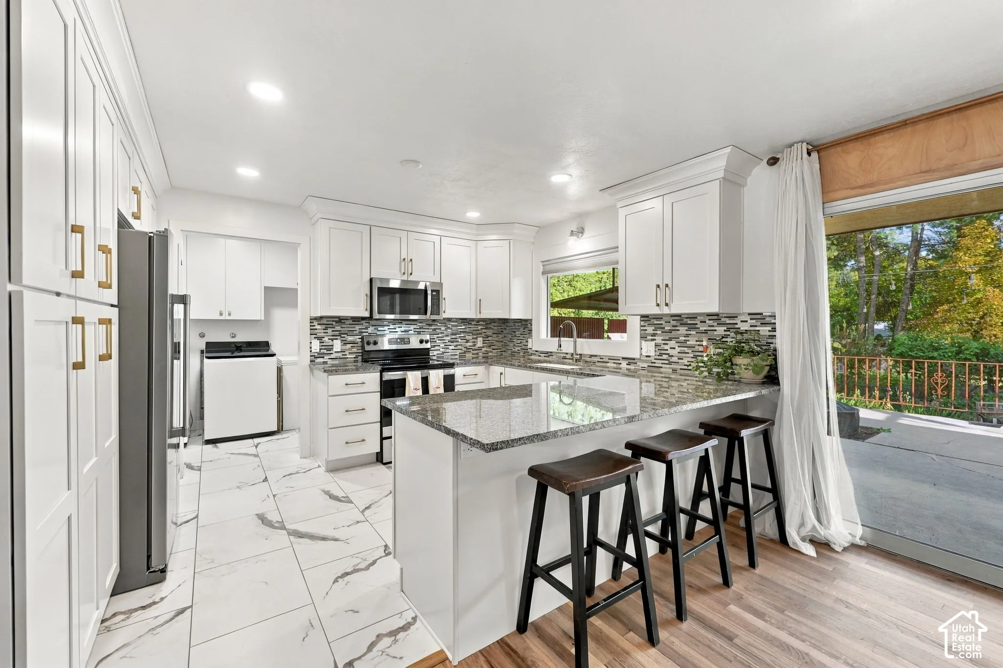 White cabinetry, stainless steel appliances, mosaic tile backsplash, granite countertops, and wood-finish flooring