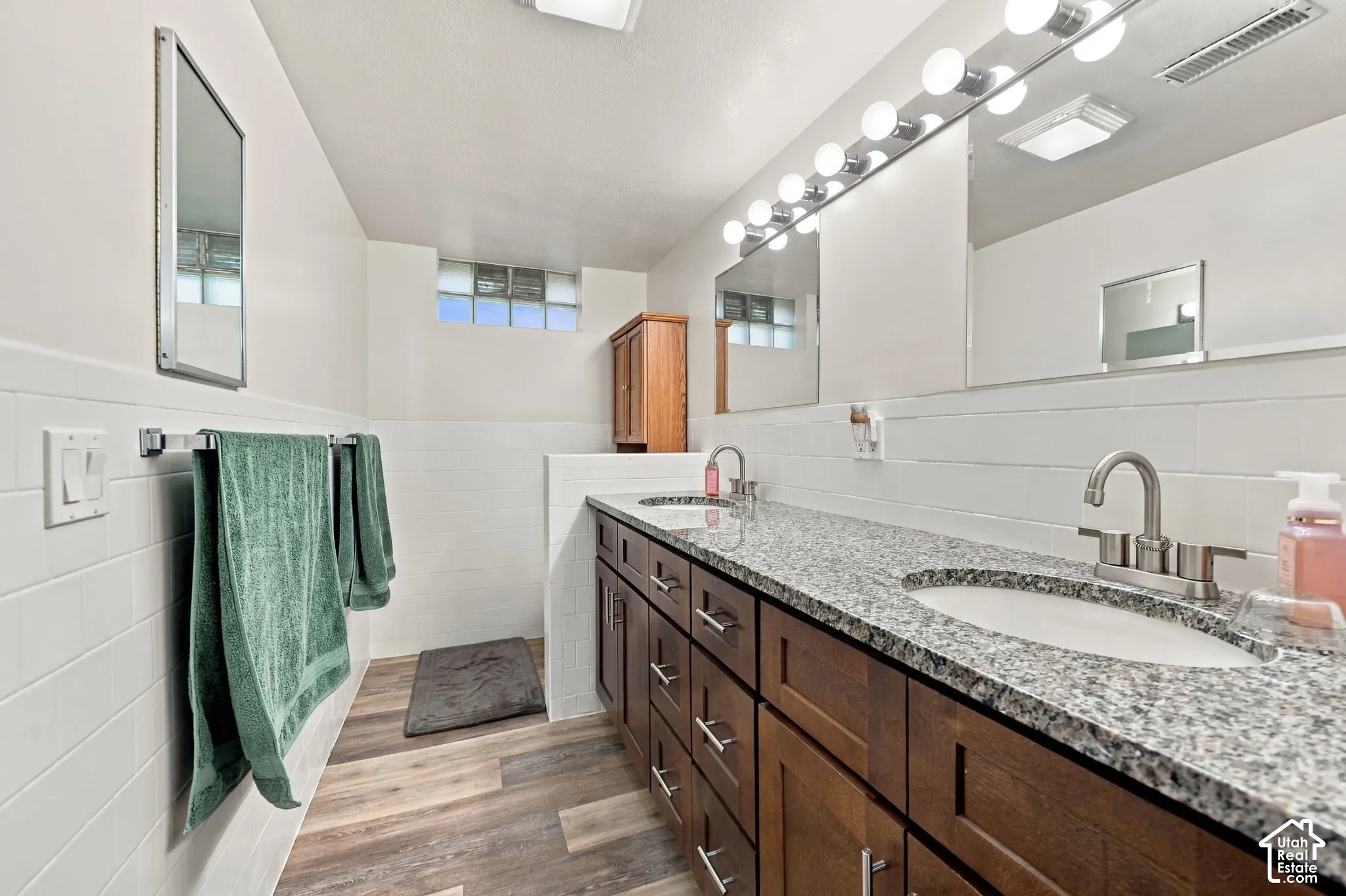 Spa-inspired primary bathroom featuring dual vanities with wood cabinetry and granite countertops, polished nickel faucets, and subway tile wainscoting