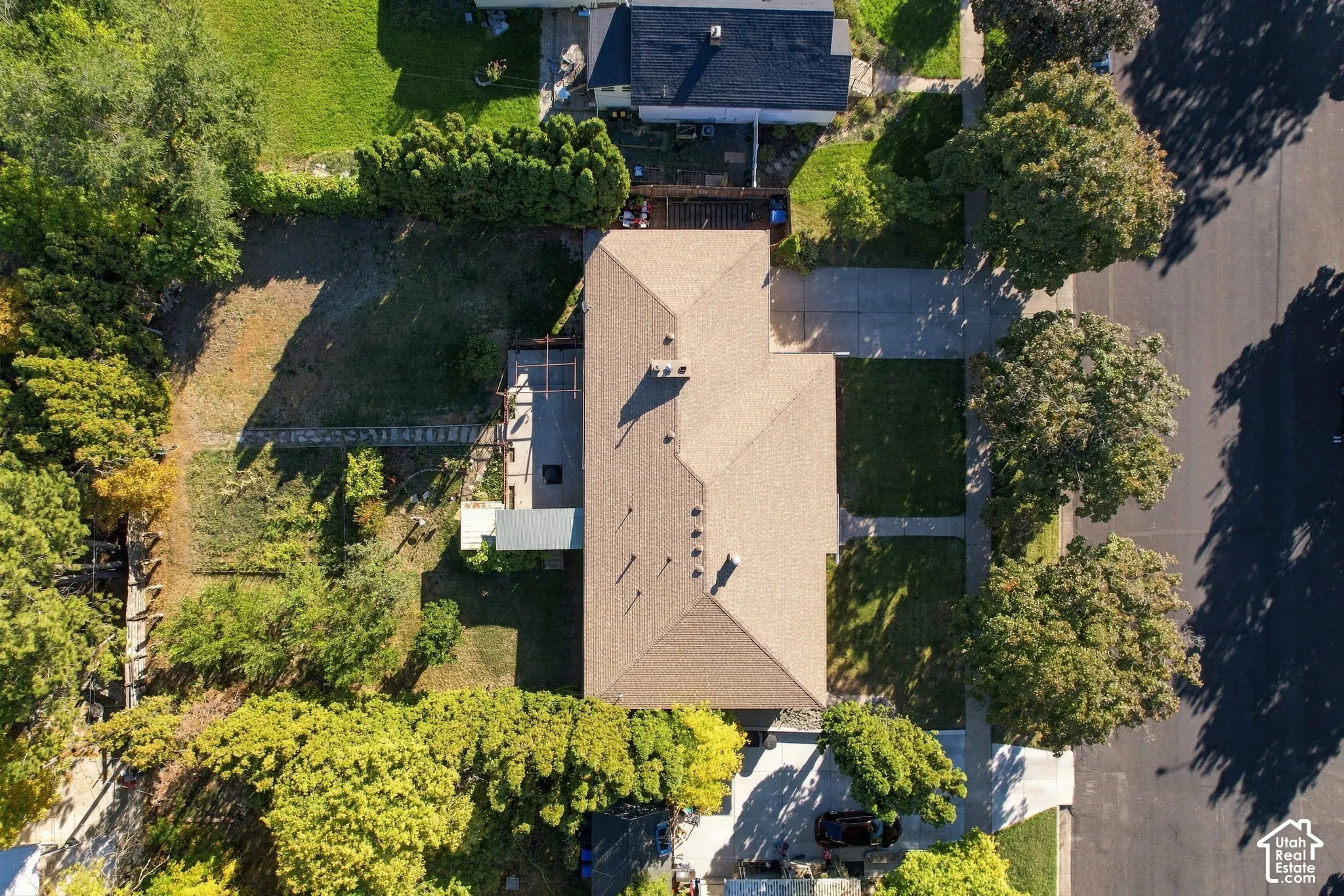 Expansive lot featuring a single-story home with a brown shingle roof, concrete driveway, front yard lawn, and established trees