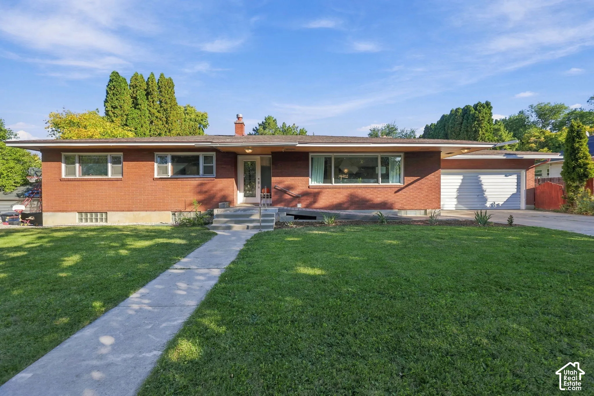 Brick Colonial home featuring a manicured front lawn, concrete walkway, and mature landscaping