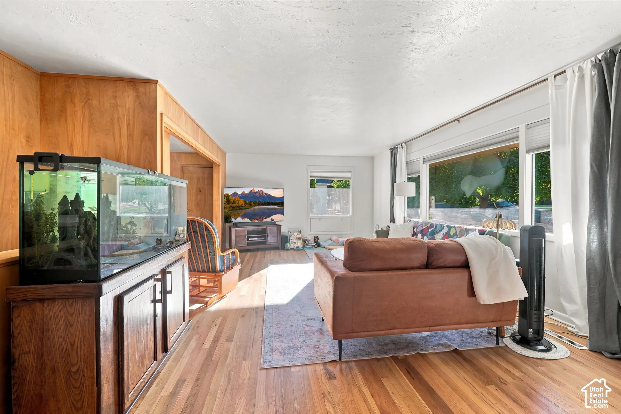 Hardwood flooring, wood paneling, wood-finish cabinetry, white painted walls, large window with blinds