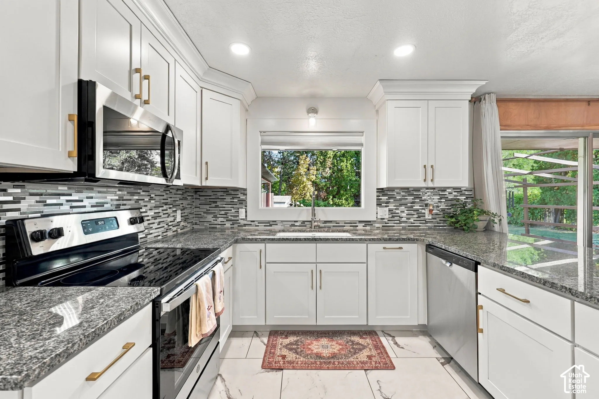 White shaker cabinetry, dark granite countertops, stainless steel appliances, mosaic tile backsplash, and recessed lighting