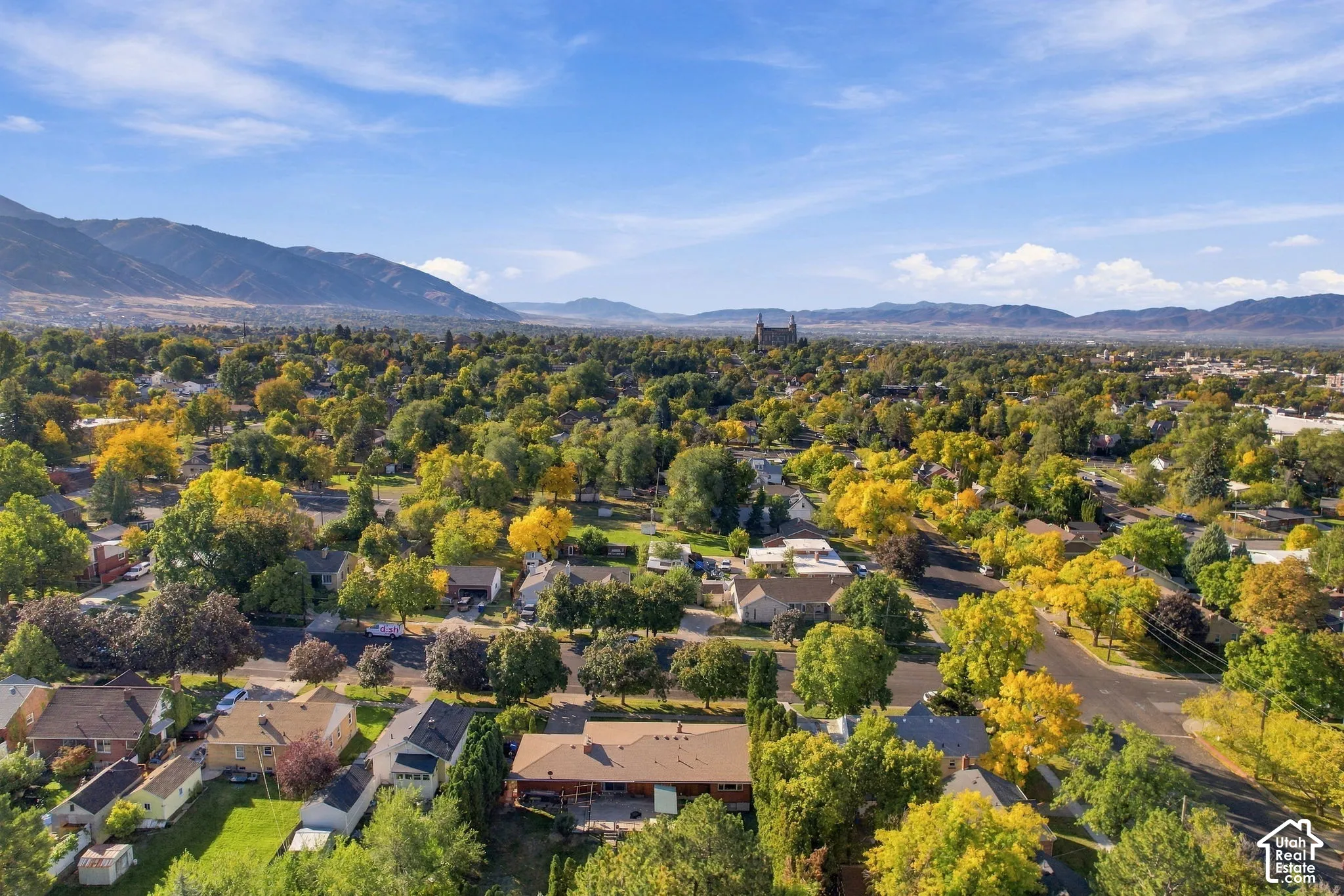 Expansive neighborhood featuring mature trees, residential properties, and distant mountain ranges under a clear sky