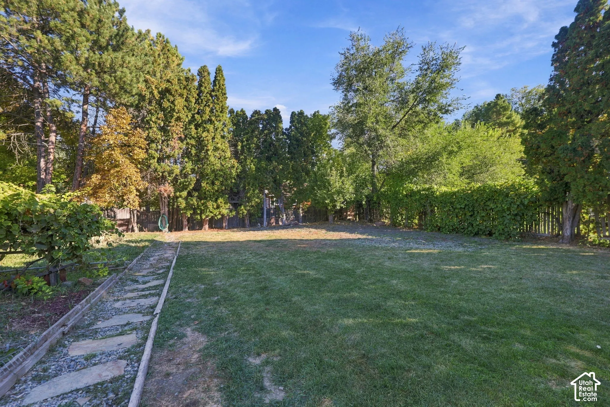 Expansive green lawn surrounded by mature trees, a stepping stone pathway, and privacy fencing