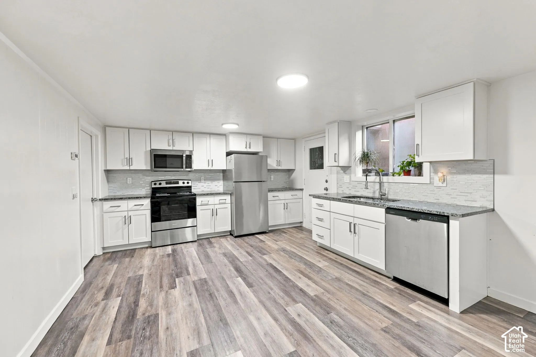 Kitchen featuring wood-finish flooring, white cabinetry, stainless steel appliances, granite countertops, and a tile backsplash