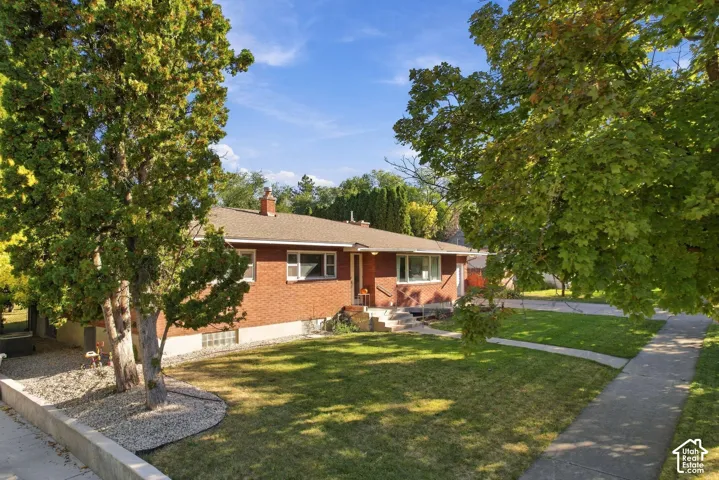 Brick exterior, gabled roof, mature trees, front lawn, concrete sidewalk