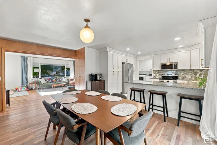 Wood-finish flooring throughout, white kitchen cabinetry, stainless steel appliances, stone-finish countertops, and a tiled kitchen backsplash