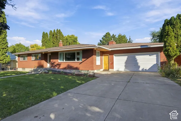 Brick exterior with a concrete driveway, attached garage, and front yard