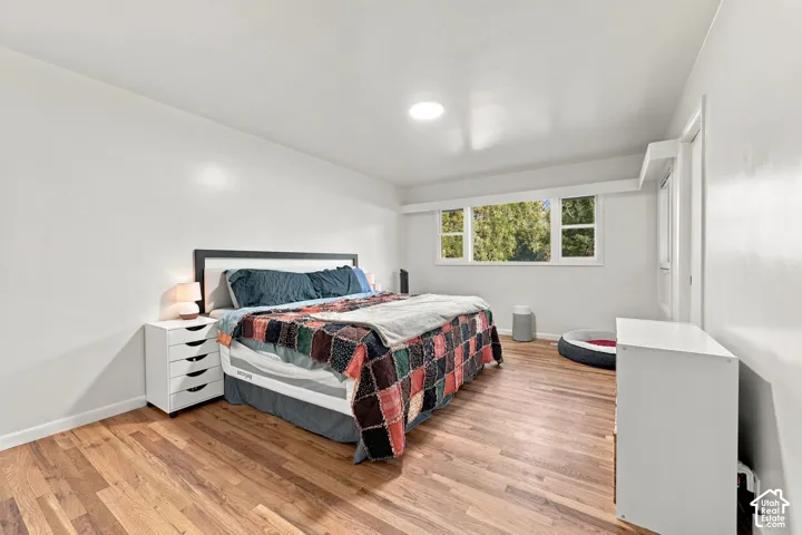 Bright bedroom with wood-finish flooring, recessed ceiling lighting, and multiple windows providing natural light