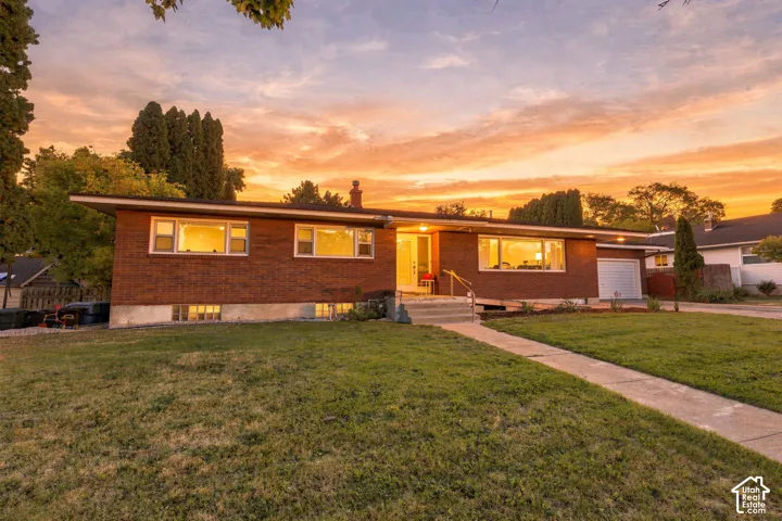 Brick exterior with multiple windows, attached garage, and a concrete walkway