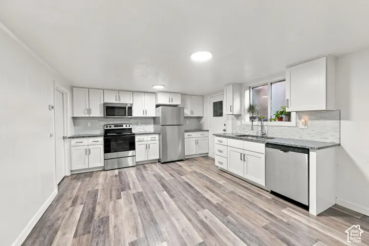 Kitchen featuring wood-finish flooring, white cabinetry, stainless steel appliances, granite countertops, and a tile backsplash