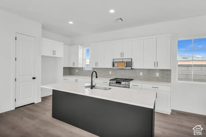 Kitchen featuring white cabinetry, a dark-toned island with a light-toned countertop, stainless steel appliances, and wood-finish flooring