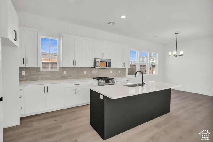 Modern kitchen featuring white shaker cabinetry, a black kitchen island with white quartz countertop, stainless steel gas range, and a black gooseneck faucet