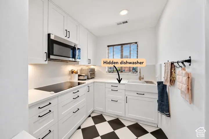 Kitchen featuring white cabinetry with matte black hardware, integrated dishwasher, apron-front sink, quartz countertops, and a black and white checkerboard tile floor