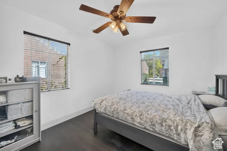 Bright secondary bedroom featuring dual windows with cellular blinds, dark wood-finish flooring, ceiling fan with integrated lighting, and built-in storage cabinetry