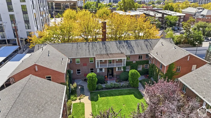Charming brick residence showcasing a private courtyard with manicured lawn, mature landscaping including topiary specimens and flowering shrubs, and mature trees providing natural canopy