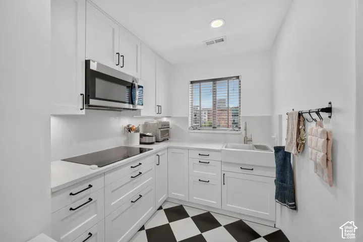 White cabinetry with matte black hardware, stainless steel microwave, integrated cooktop, white farmhouse sink, and checkerboard floor tiling