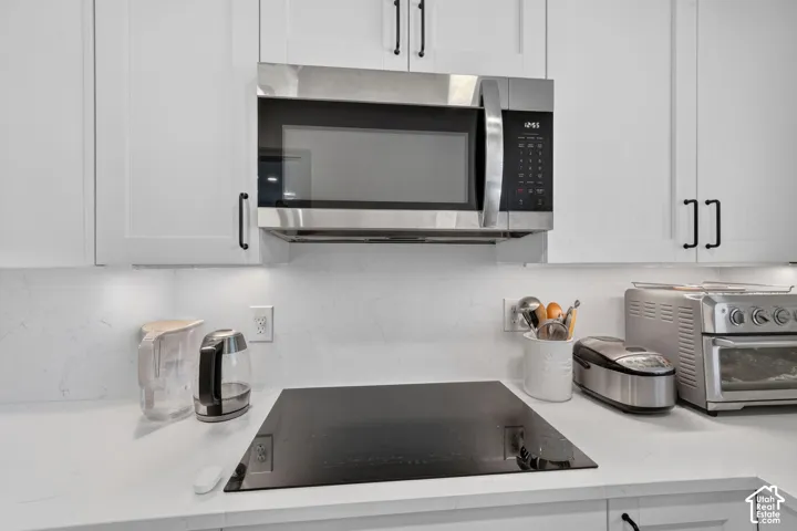 Modern kitchen featuring stainless steel over-the-range microwave, sleek black cooktop with white quartz countertops, white shaker-style cabinetry with brushed nickel hardware, and integrated appliances including a convection oven and stainless steel smal