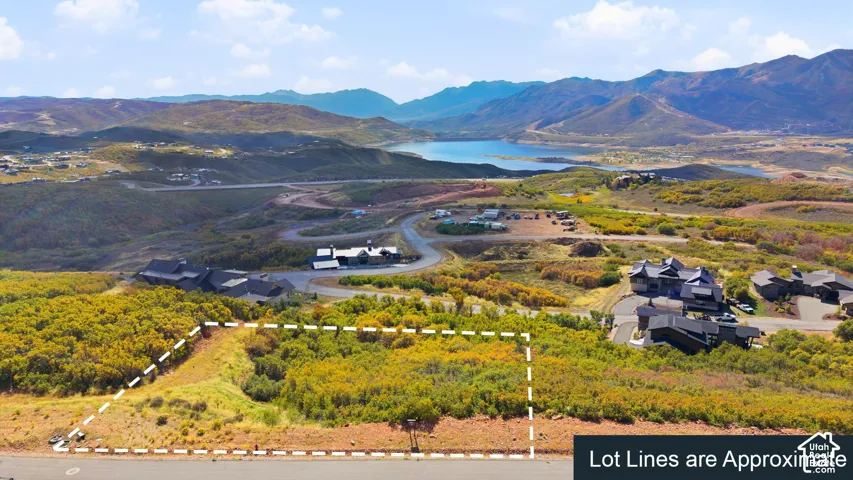 Expansive building lot featuring natural vegetation, surrounded by mountainous terrain, with distant water visible, and adjacent to paved roadways