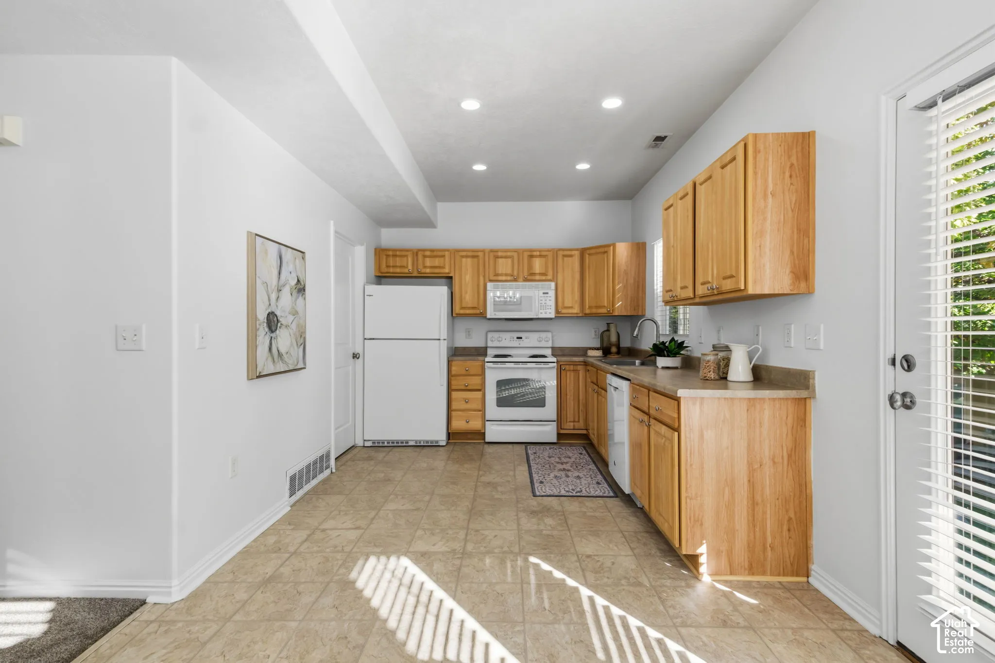 Kitchen featuring light wood cabinetry, white appliances, and a light-toned tile floor