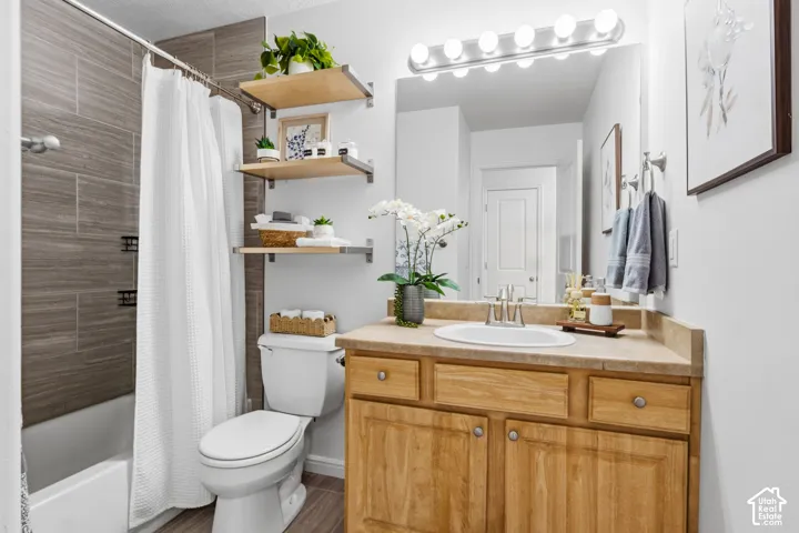Full bathroom featuring a shower-tub combination with tile surround, wood-finish flooring, a vanity with wood cabinetry, and a large mirror with overhead lighting