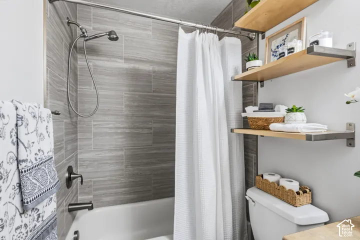 Bathtub with tiled shower surround, brushed nickel fixtures, and wall-mounted shelving