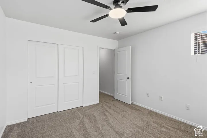 Neutral wall color, ceiling fan with integrated lighting, window with horizontal blinds, textured carpet, and a white paneled door