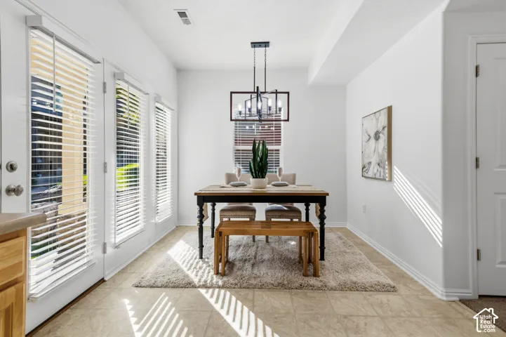 Recessed ceiling, neutral wall paint, tile flooring, modern chandelier, and multiple windows with blinds