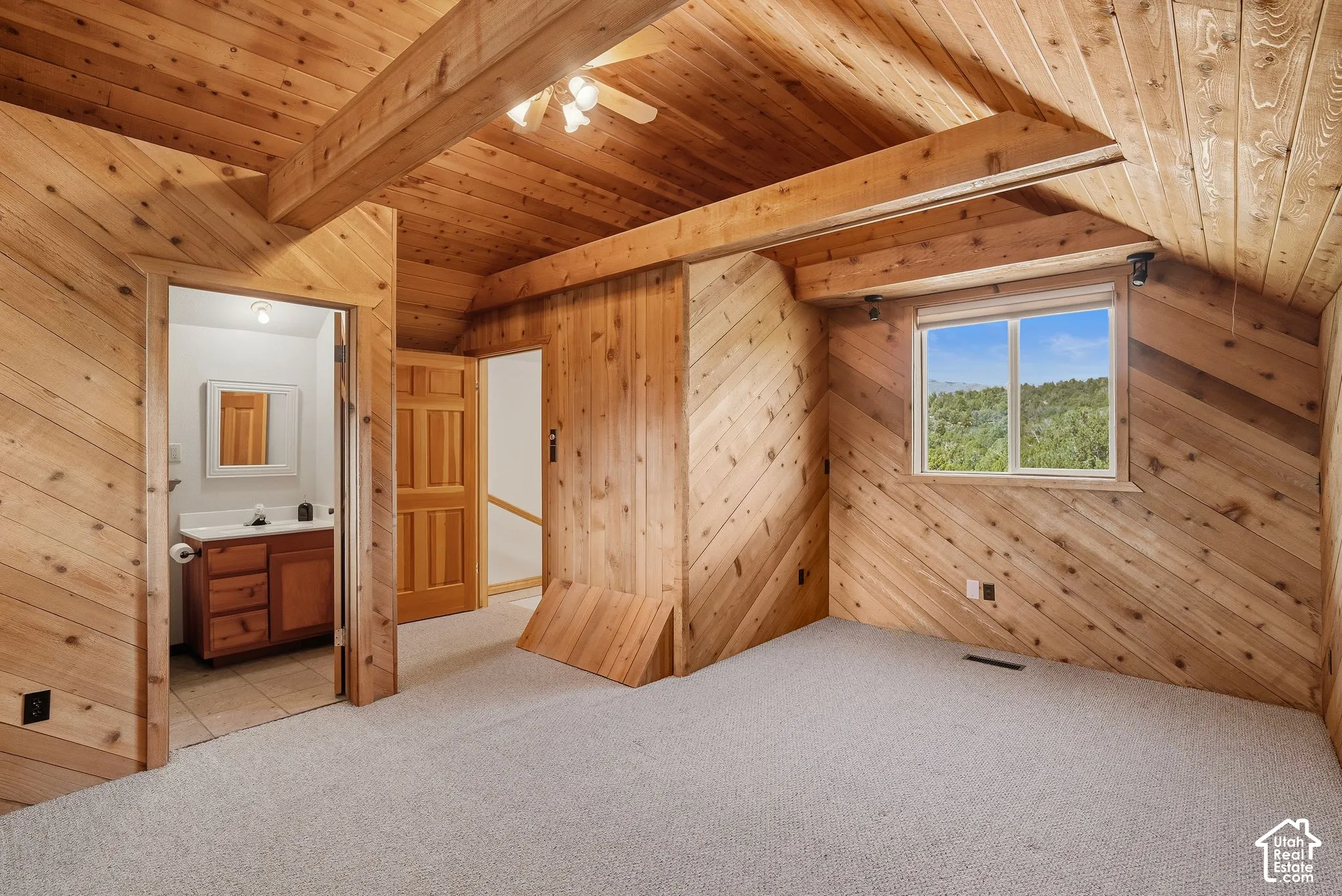 Spacious upper-level bedroom showcasing cathedral ceilings with exposed wood beams, knotty pine walls and ceiling, and generous natural light from a large picture window
