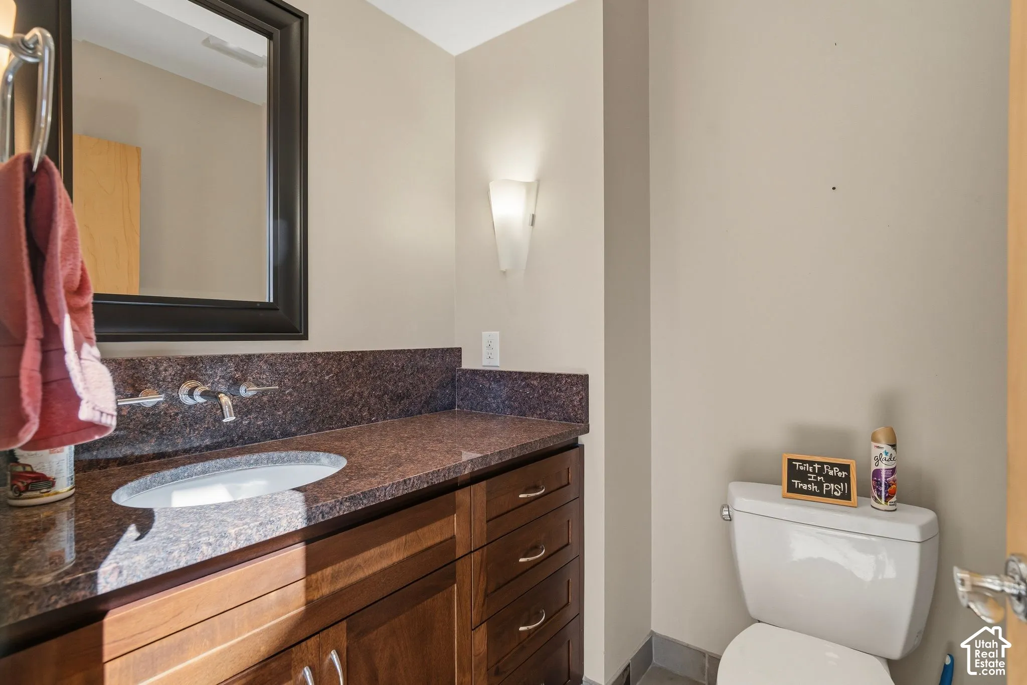 Spa-inspired bathroom featuring a wood-finish vanity with dual vessel sinks, dark speckled stone countertops, and framed mirror with integrated lighting