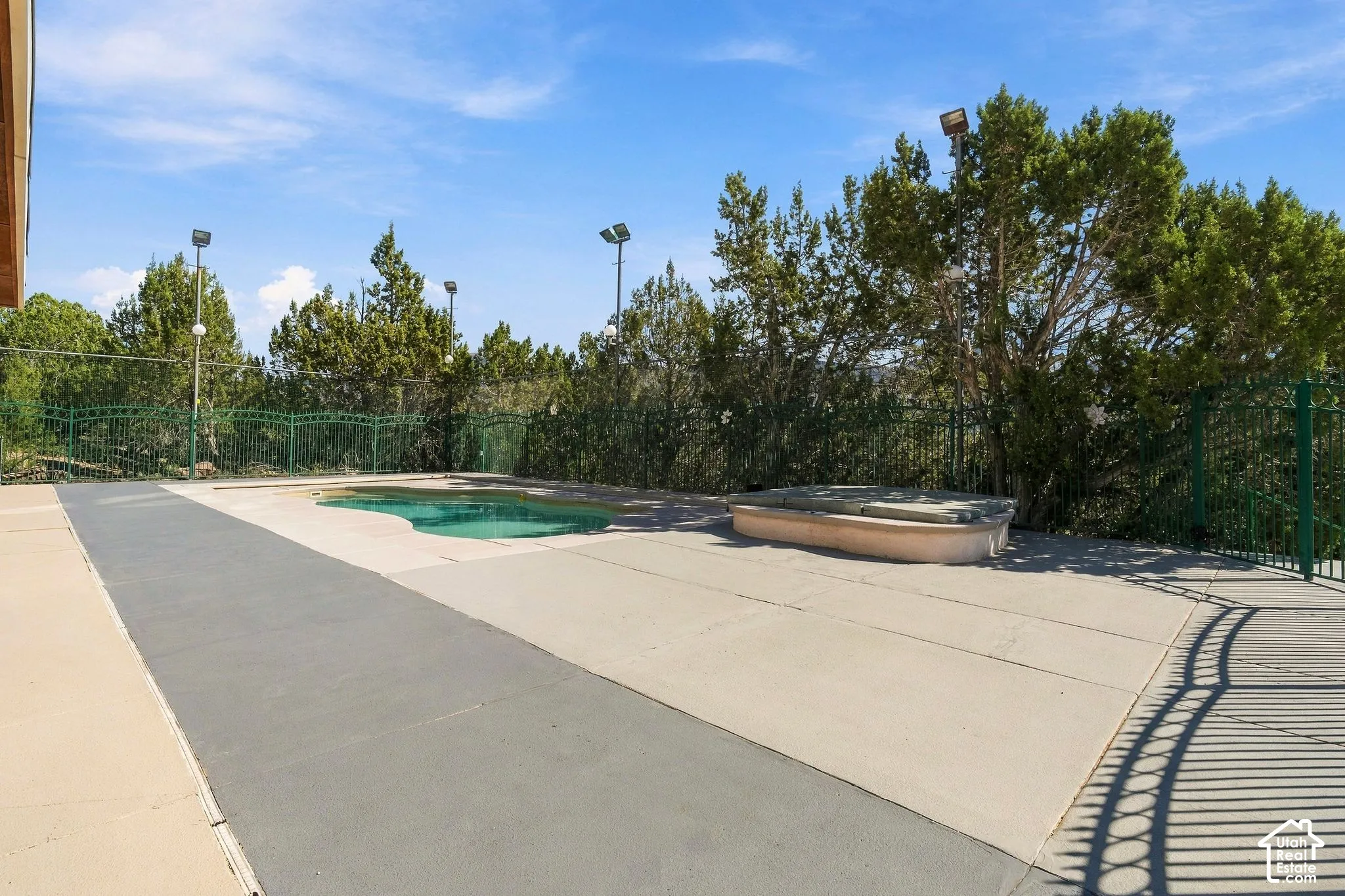 Outdoor pool with a light-colored concrete surround, an integrated spa, and a perimeter fence