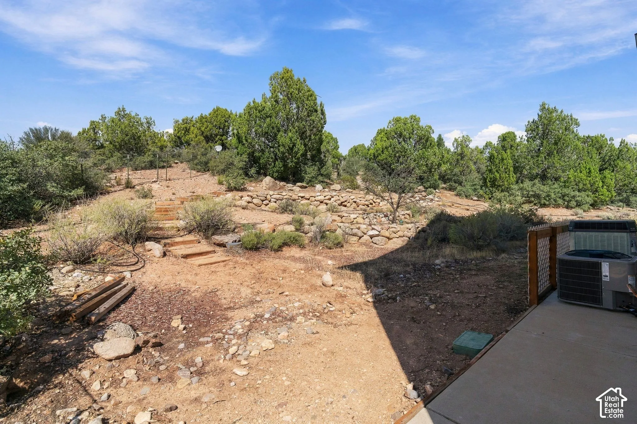 Expansive outdoor space featuring a concrete patio, wood-framed privacy screen, and natural landscaping with mature trees and shrubs