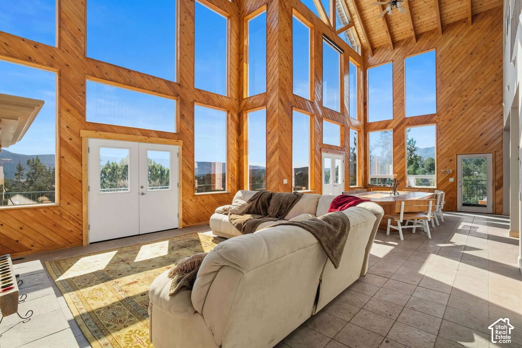 Vaulted wood-paneled ceiling, extensive multi-paned windows, double glass doors, wood-finish dining table, and stone-look flooring